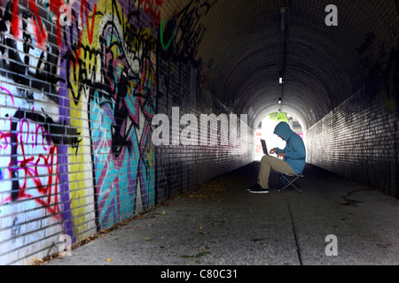 Computer-Benutzer, Hacker, verschwörerisch, in einem Tunnel mit einem Laptop sitzt. Symbolbild, Computer-Internet-Kriminalität. Stockfoto