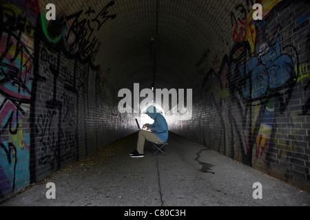 Computer-Benutzer, Hacker, verschwörerisch, in einem Tunnel mit einem Laptop sitzt. Symbolbild, Computer-Internet-Kriminalität. Stockfoto