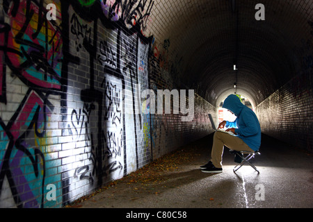 Computer-Benutzer, Hacker, verschwörerisch, in einem Tunnel mit einem Laptop sitzt. Symbolbild, Computer-Internet-Kriminalität. Stockfoto