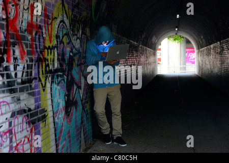 Computer-Benutzer, Hacker, verschwörerisch, in einem Tunnel mit einem Laptop sitzt. Symbolbild, Computer-Internet-Kriminalität. Stockfoto