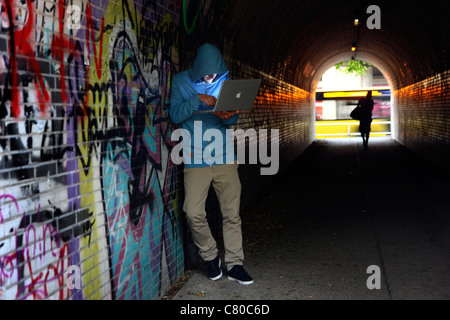 Computer-Benutzer, Hacker, verschwörerisch, in einem Tunnel mit einem Laptop sitzt. Symbolbild, Computer-Internet-Kriminalität. Stockfoto
