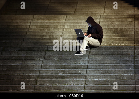 Computer-Benutzer, Hacker, verschwörerisch, sitzt draußen, auf Treppen, mit einem Laptop. Symbolbild, Computer-Internet-Kriminalität. Stockfoto