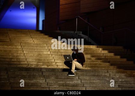 Computer-Benutzer, Hacker, verschwörerisch, sitzt draußen, auf Treppen, mit einem Laptop. Symbolbild, Computer-Internet-Kriminalität. Stockfoto