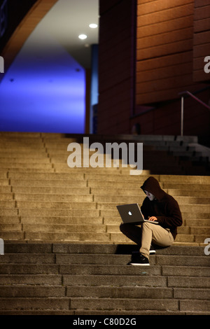 Computer-Benutzer, Hacker, verschwörerisch, sitzt draußen, auf Treppen, mit einem Laptop. Symbolbild, Computer-Internet-Kriminalität. Stockfoto