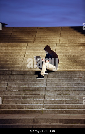 Computer-Benutzer, Hacker, verschwörerisch, sitzt draußen, auf Treppen, mit einem Laptop. Symbolbild, Computer-Internet-Kriminalität. Stockfoto