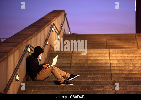 Computer-Benutzer, Hacker, verschwörerisch, sitzt draußen, auf Treppen, mit einem Laptop. Symbolbild, Computer-Internet-Kriminalität. Stockfoto