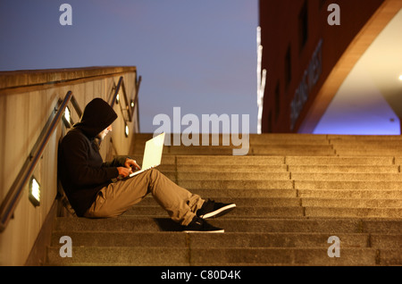 Computer-Benutzer, Hacker, verschwörerisch, sitzt draußen, auf Treppen, mit einem Laptop. Symbolbild, Computer-Internet-Kriminalität. Stockfoto