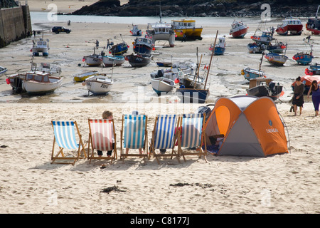 Urlauber auf Liegestühlen mit einem Beach Shelter Zelt im Hafen von St. Ives, Cornwall. Stockfoto