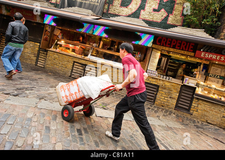 London Camden Lock Stables Markt jungen asiatischen Orientalisch männlich Mann liefert Säcke Reis auf Wagen Lkw Barrow fast food Stände Creperie Pizza Stockfoto