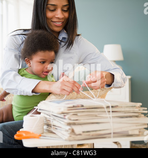 African American Mutter halten Baby auf Schoß und binden Zeitungen Stockfoto