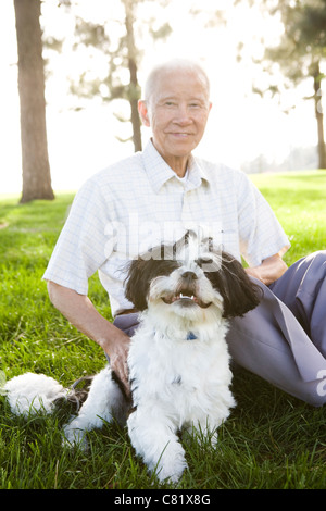 Hochrangige chinesische Mann sitzt in Grass mit Shih Tzu Hund Stockfoto