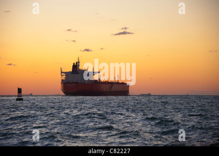 Frachtschiff verlassen Hafen bei Sonnenuntergang Stockfoto