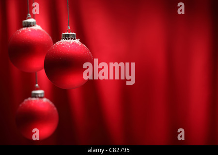 Rote Weihnachtskugeln hängen über rotem Grund. Stockfoto