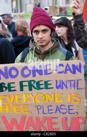 Ein Mann hält ein Protest Schild mit der Aufschrift "Niemand kann frei sein, bis alle frei ist.  Bitte aufwachen "während Occupy Wall Street Stockfoto