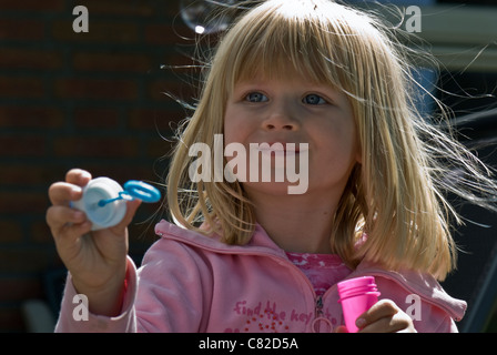 Seifenblase, die kleine blonde Mädchen trägt eine rosa Jacke bewundern ihre Seifenblasen weht Stockfoto