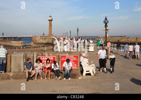 Eine Familie Essen Fish And Chips mit Whitby Pier im Hintergrund. Stockfoto