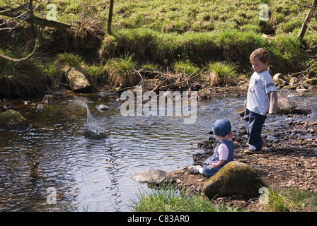 Kleine Jungen und Mädchen spielen, werfen Kieselsteine in den Fluss, Hathersage, Peak District, Derbyshire, UK Stockfoto