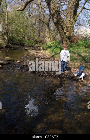 Kleine Jungen und Mädchen spielen, werfen Kieselsteine in den Fluss, Hathersage, Peak District, Derbyshire, UK Stockfoto