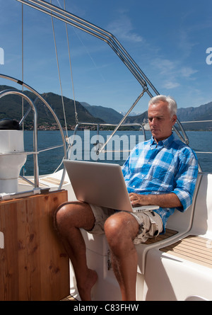 Älterer Mann mit Laptop auf Segelboot Stockfoto