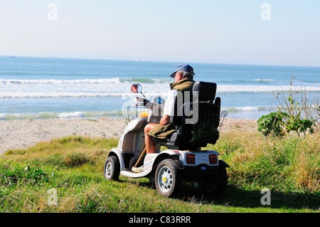Behinderter Mann im Mobilitätsroller mit Blick auf den Solent aus dem Grünsward am West Wittering Beach, in der Nähe von Chichester, West Sussex, England, Großbritannien Stockfoto