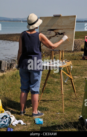 Künstlerin stehen und malen mit Ölen an Staffelei an Eleanor Punkt, Chichester Harbour, West Wittering, West Sussex, UK Stockfoto