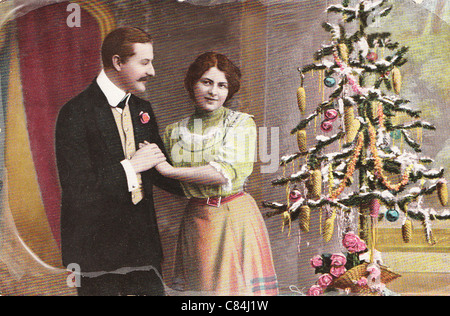 Vintage Weihnachtsgrußkarte von 1910 mit Liebespaar in der Nähe von Kleinbaum Stockfoto