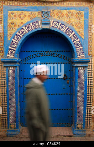 Marokkanischen Mann gekleidet in traditionellen Jellabah Spaziergang vorbei an einer bunten Holz & geflieste Tür in der Medina, Essaouira, Nordafrika Stockfoto