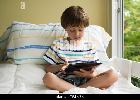 Junge sitzt auf dem Bett, mit digital-Tablette Stockfoto