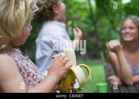 Kleines Mädchen im Freien mit ihrer Familie, Banane essen Stockfoto