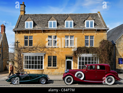 Zwei klassische Autos parkten außerhalb eines historischen Gebäudes, Broadway, Cotswolds. Erhältlich in Farbe oder schwarz / weiß. Stockfoto