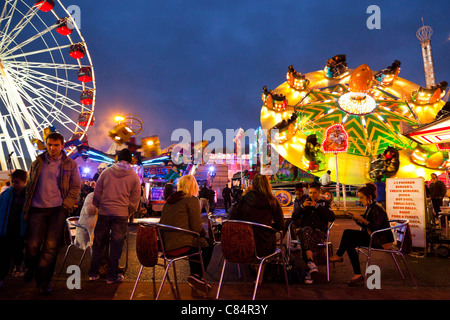 Menschen sitzen unter Fahrgeschäfte in der Nacht bei Goose Fair, Nottingham, England, Großbritannien Stockfoto