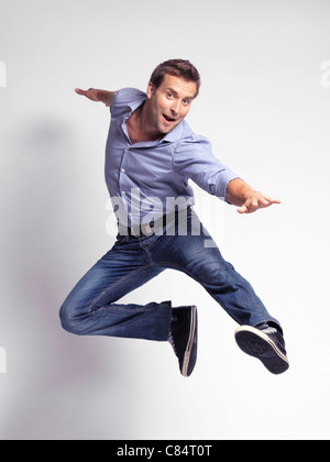 Glücklich springen jungen Mann trägt Jeans und ein Hemd auf grauem Hintergrund isoliert Stockfoto