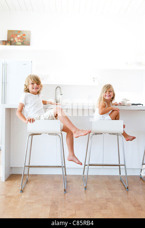 Bruder und Schwester sitzen auf Hockern in weiße Küche Stockfoto