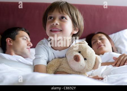 Junge sitzt im Bett der Eltern umarmt Teddybär Stockfoto