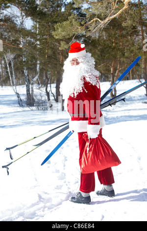 Porträt von Santa Claus mit Skiern und Plünderung von Geschenken Stockfoto