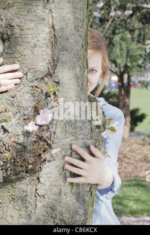 Frau spähen aus hinter Baum Stockfoto