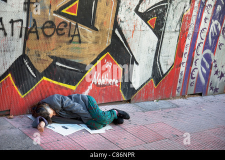 Die Menschen gehen vorbei an eine Obdachlose Frau auf der Straße schlafen. Die Kluft zwischen Arm und Reich in Omonia, Athen ein alltäglicher Anblick. Stockfoto