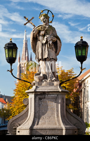 Statue von St. Johannes von Nepomuk, Sint-Jan Nepomucenus auf Wollestraat Brücke in Brügge. Turm der Kirche unserer lieben Frau im Hintergrund. Stockfoto
