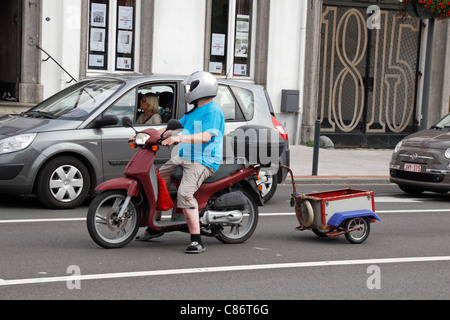 Lässig gekleidet Mann auf einem Honda Motorroller mit angehängten Anhänger in der Stadt von Waterloo, Belgien. Stockfoto