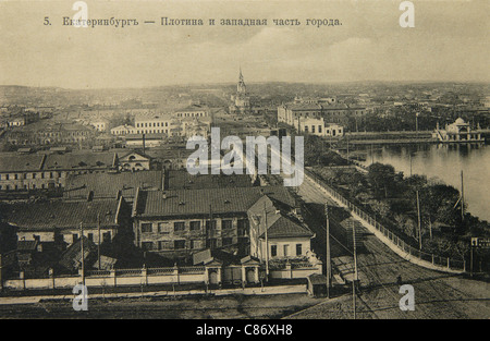 Fabrikdamm und die westlichen Viertel von Jekaterinburg, Russisches Reich. Schwarz-Weiß-Vintage-Fotografie des russischen Fotografen Veniamin Metenkov vom Anfang des 20. Jahrhunderts, herausgegeben in der russischen Vintage-Postkarte, die von Veniamin Metenkov selbst in Jekaterinburg herausgegeben wurde. Der Werksdamm am Iset wurde 1723 für die Jekaterinburg Metallverarbeitung gebaut. Die Gebäude der Fabrik sind links zu sehen. Das Gebäude in der Mitte des Bildes ist das Hauptgebäude der Jekaterinburg Lapidarium Fabrik. Die Kathedrale der Kreuzerhöhung auf der Kathedrale Stockfoto