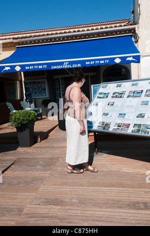 Eine Frau schaut Details zu Ferienhäuser zum Verkauf oder zur Miete außerhalb eines Immobilienmakler in Marseillan, Südfrankreich. Stockfoto