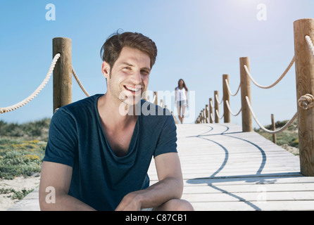 Spanien, Mallorca, junger Mann sitzt auf Promenade und Frau zu Fuß im Hintergrund Stockfoto