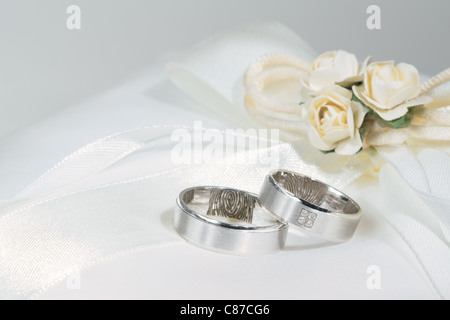 Trauringe auf einem weißen sating Träger Ringkissen mit Blumen. Stockfoto