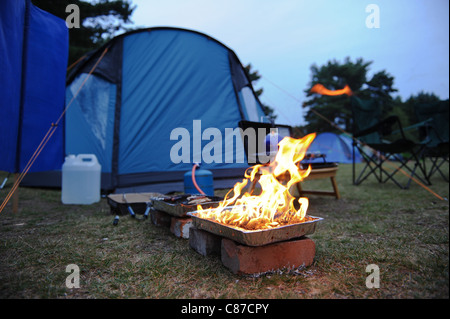 ein Barbecue beleuchtet neben einem Zelt mit verschiedenen Kochgeräte rund um camping Essen vorbereiten Stockfoto