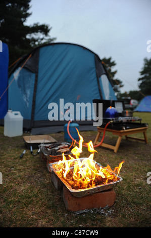 Grill beleuchtet neben Zelt mit verschiedenen Kochgeräte für camping Stockfoto