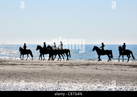 Reiten am Strand in Silhouette in West Wittering nr. Chichester, West Sussex, England Stockfoto
