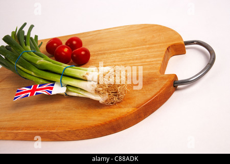 Frühlingszwiebeln mit Cherry-Tomaten auf Schneidebrett Stockfoto