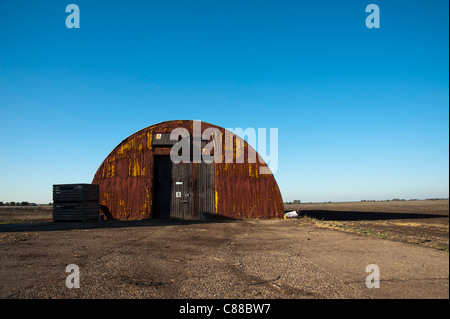 Nissen-Hütte in der flachen Landschaft der Fens in Cambridgeshire leuchtet wunderschön Seite vor einem atemberaubenden blauen Himmel. Stockfoto