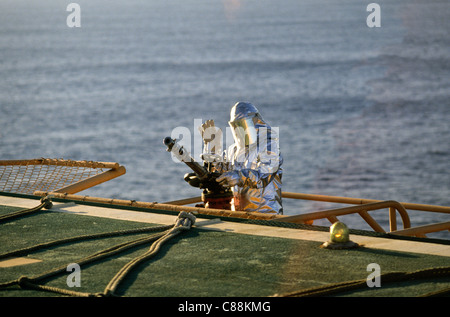 Rio De Janeiro, Brasilien. Oil Rig Arbeiter in Silber feuerfesten Anzug und Helm mit Visier und Wasserwerfer Feuerwehrschlauch. Stockfoto