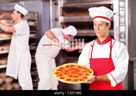 Männliche Bäcker hält frisch gebackene Pizza in Bäckerei Stockfoto